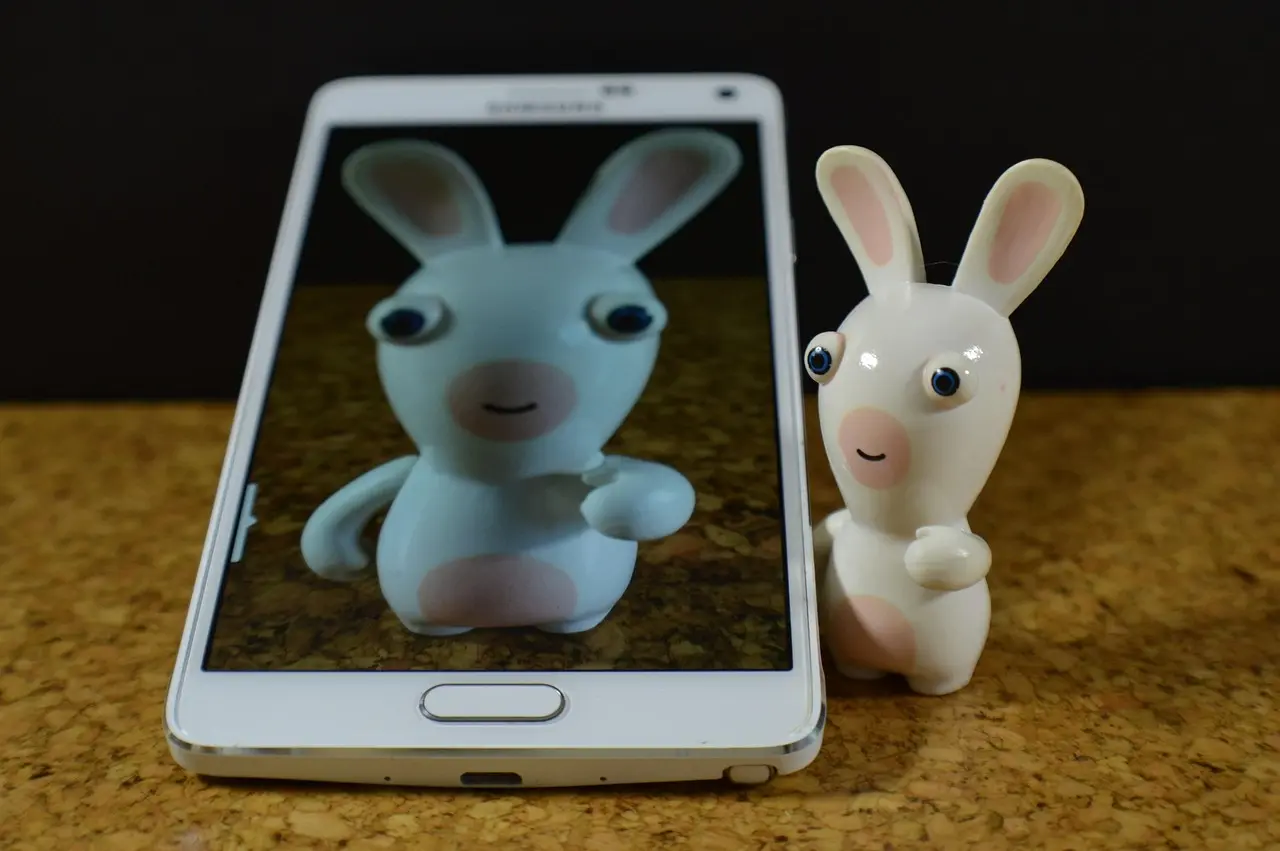 biały smartfon Samsung z porcelanowym królikiem na wyświetlaczu i obok niego.